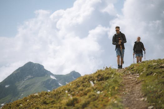 A couple enjoying a hike through lush mountains with trekking poles under a cloudy sky.